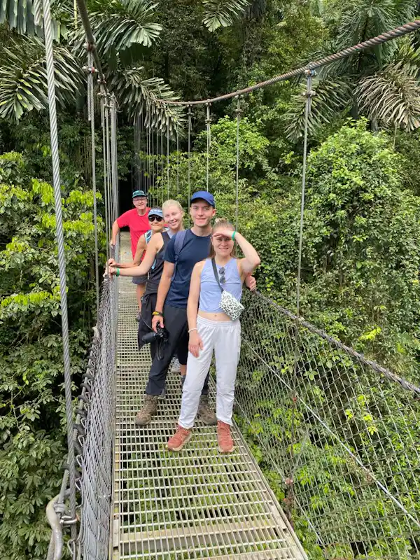 Adventure travelers crossing a long suspension bridge over the tropical valley